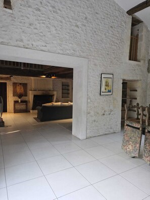 A spacious living area with a high ceiling and exposed wooden beams, a fireplace, and a large window. - Country house Berneuil (17460) (Berneuil)