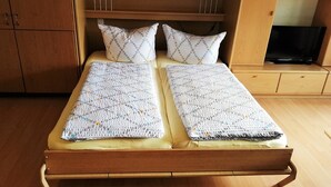 A double bed with a patterned blanket, two pillows, a wooden headboard, and a television on a wooden stand. - Sommerhof Rauber – Studio 'A 03' with Lake View, Shared Garden and Wi-Fi (Immenstaad am Bodensee)