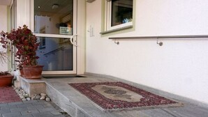 A building entrance with a glass door, a potted plant, a small rug, and a window with a green frame. - Sommerhof Rauber – Studio 'A 03' with Lake View, Shared Garden and Wi-Fi (Immenstaad am Bodensee)