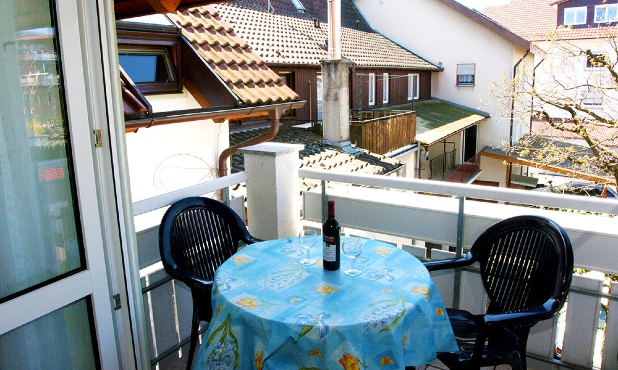 Un balcón con una mesa y sillas, una botella de vino y vistas a casas cercanas.