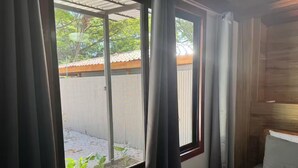 A room with a bed, a window with curtains, and a view of a garden and a fence. - Beautiful Casa Azul (Potrero)