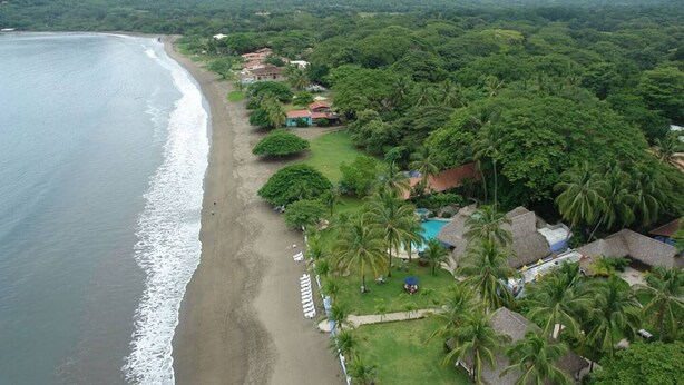 An aerial view of a coastal resort with a beach, palm trees, and thatched-roof buildings. - Beautiful Casa Azul (Potrero)