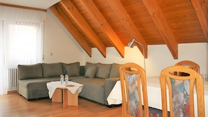 A loft-style room with a wooden ceiling, a sofa, a small table with bottles, and a chair. - Sommerhof Rauber – Apartment 'B 04' with Lake View, Shared Garden and Wi-Fi (Immenstaad am Bodensee)