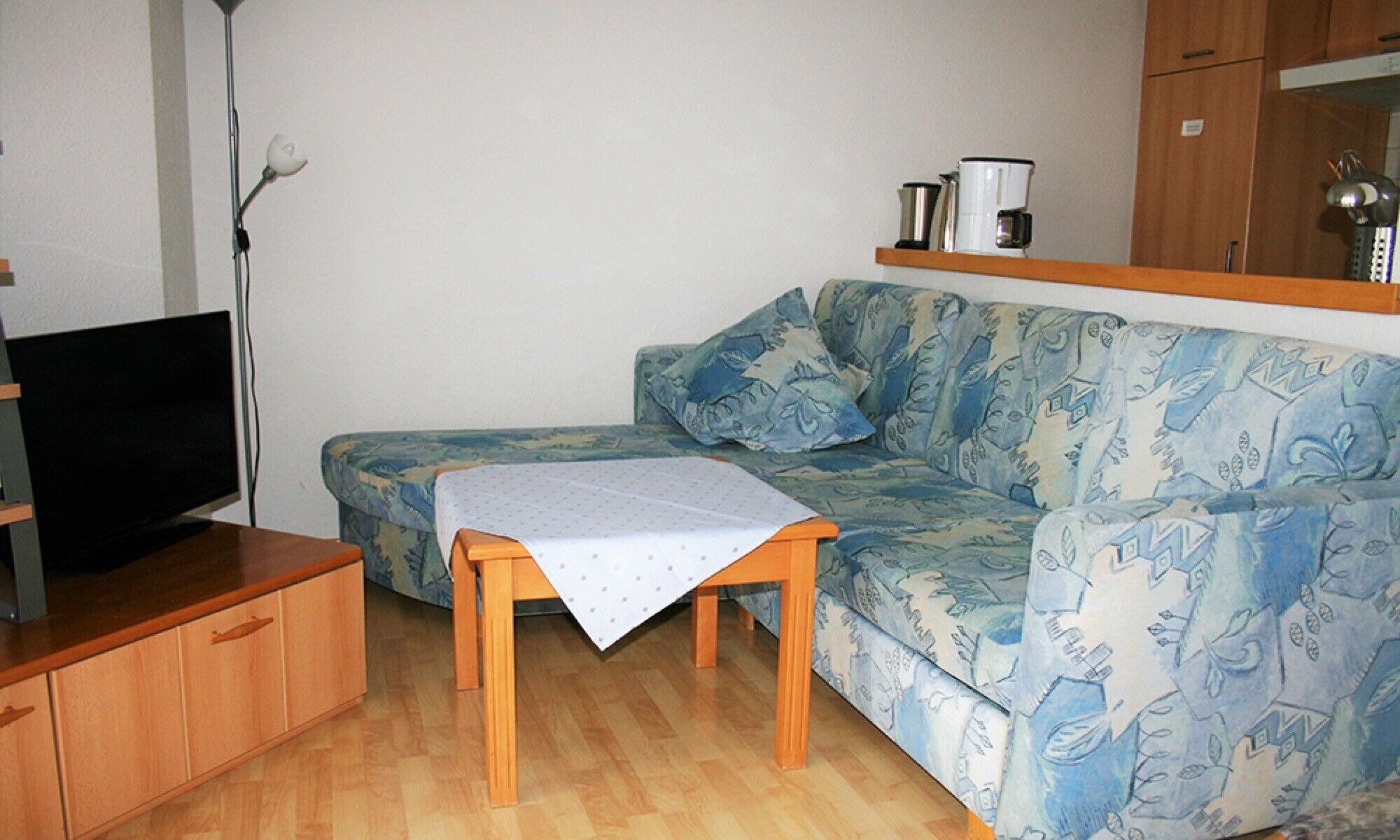 A small living area with a sofa, a television, a coffee maker, and a lamp.