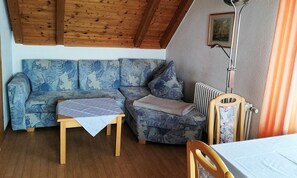 Una habitación acogedora con techo de madera, un sofá estampado, una mesita, un radiador y una silla.
