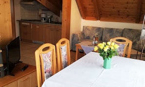 Un comedor con una mesa, sillas, un jarrón de flores, un sofá y una cocina al fondo.