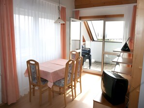 A dining area with a table and chairs, a television, and a view of the outside.