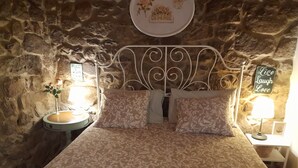 A cozy bedroom with a stone wall, a metal bed frame, and a bed with patterned bedding. There are two bedside tables with lamps and a sign that says "Live Laugh Love." - Casa Maínha Solar Minhoto Century XVII with private pool  (Panóias)