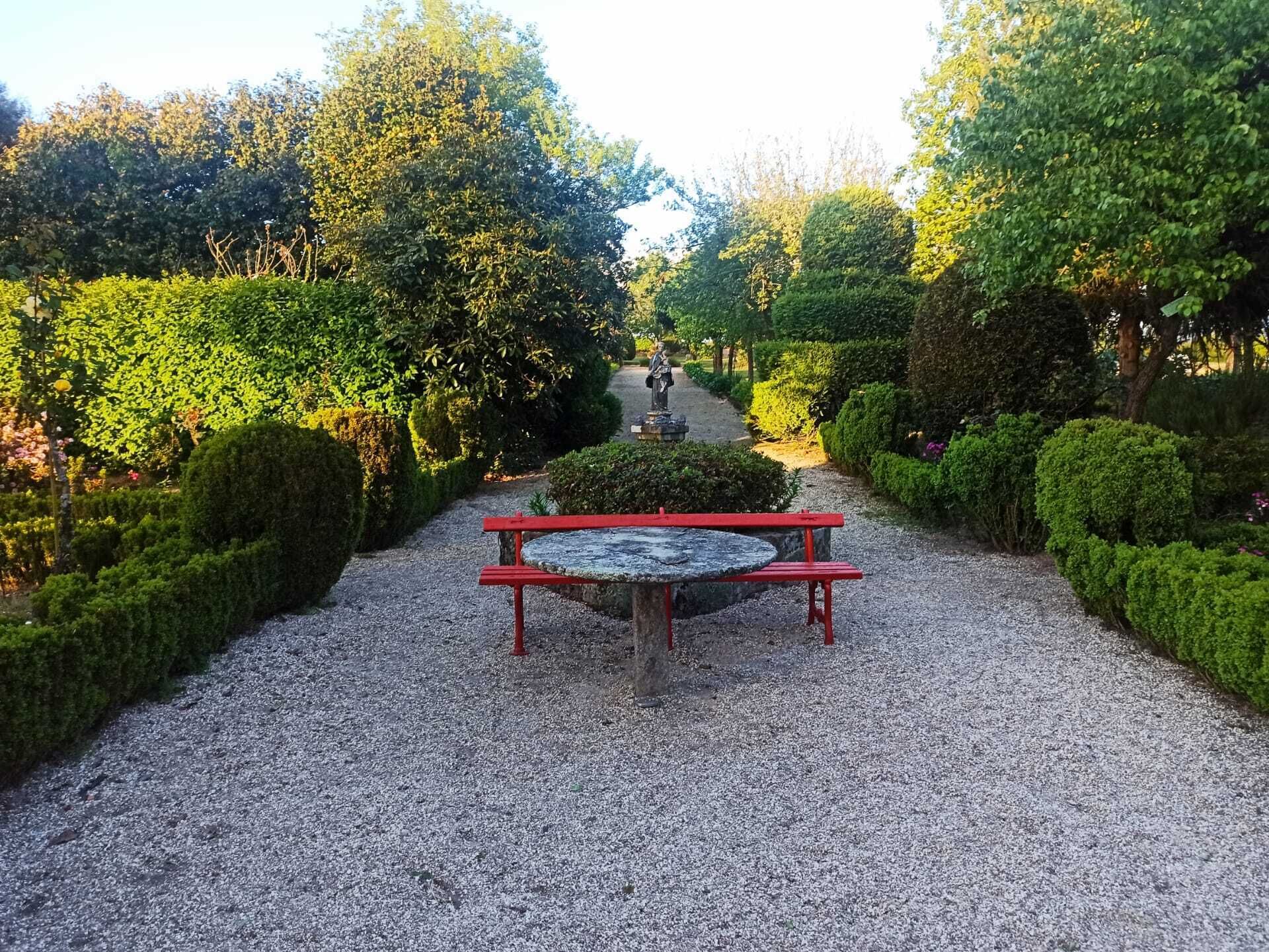A gravel pathway with a red bench and a statue in a garden setting.