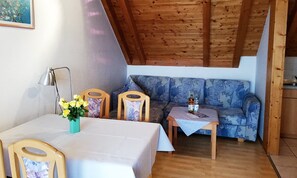 Um quarto aconchegante com teto de madeira, um sofá, uma mesinha com bebidas e uma cadeira com um vaso de flores.