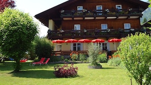 A multi-story wooden building with balconies, red umbrellas, and a well-maintained garden with red flowers and green shrubs.