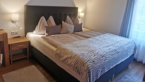 A bedroom with a bed, nightstands, a wooden ceiling, and a window with curtains.