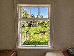 Una habitación con ventana que da a un área verde con una bicicleta y una mesa de picnic.