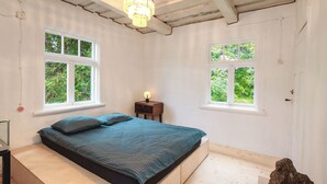 Une chambre à coucher avec un lit, deux fenêtres, une table de chevet et un lustre.