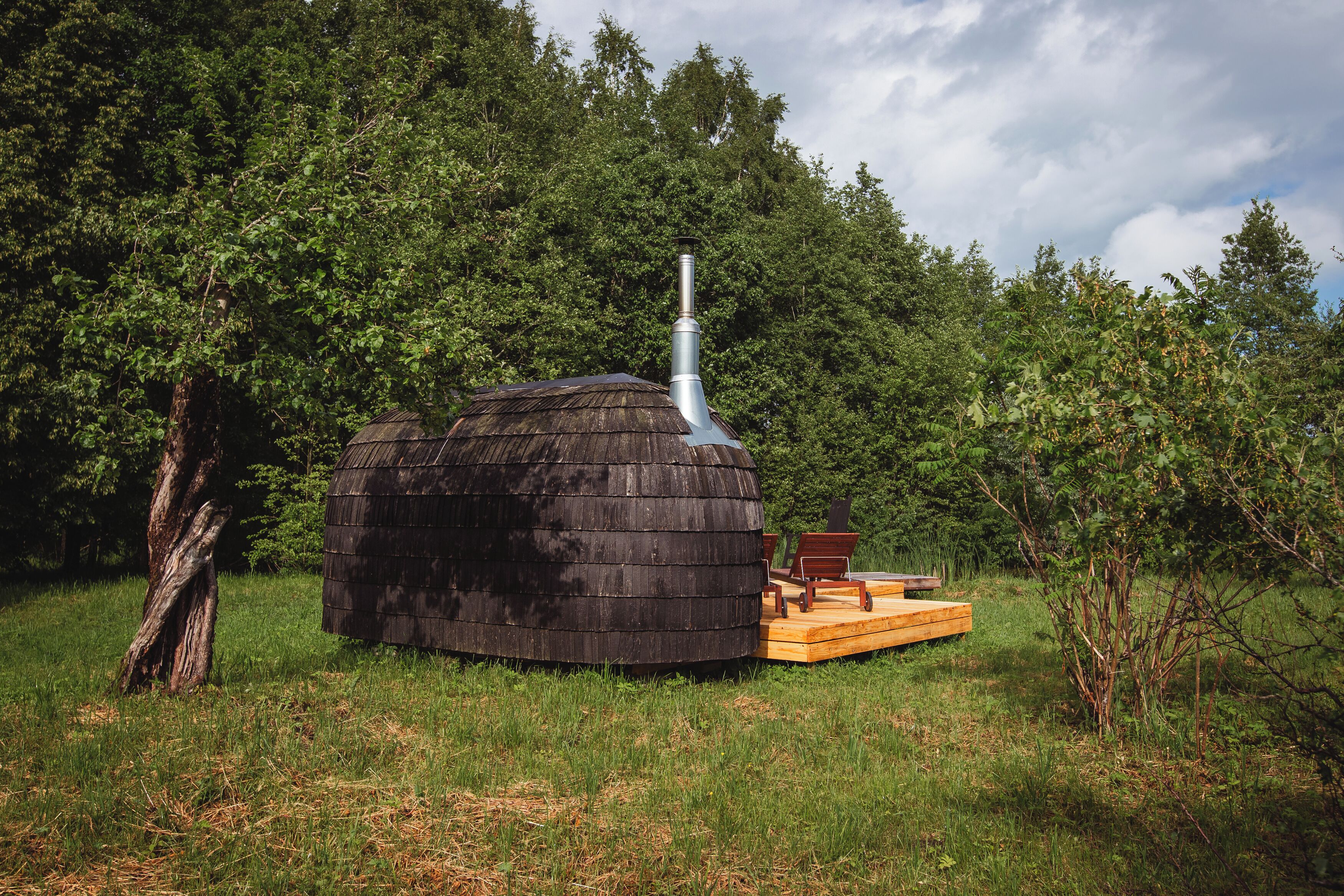 A rustic wooden cabin with a chimney, surrounded by dense greenery.