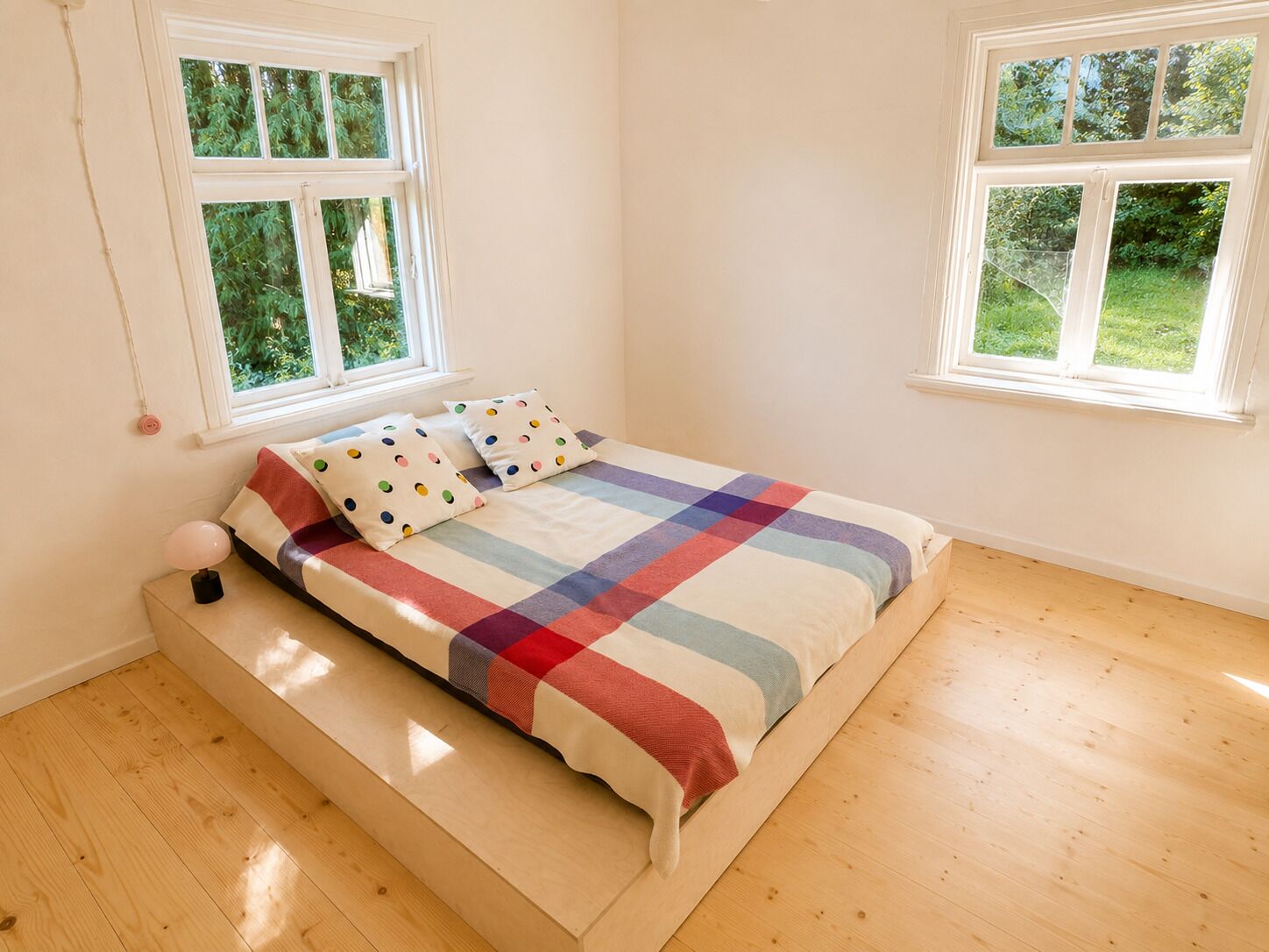 A bedroom with a bed, two windows, and a wooden floor.