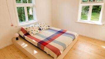 A bedroom with a bed, two windows, and a wooden floor.