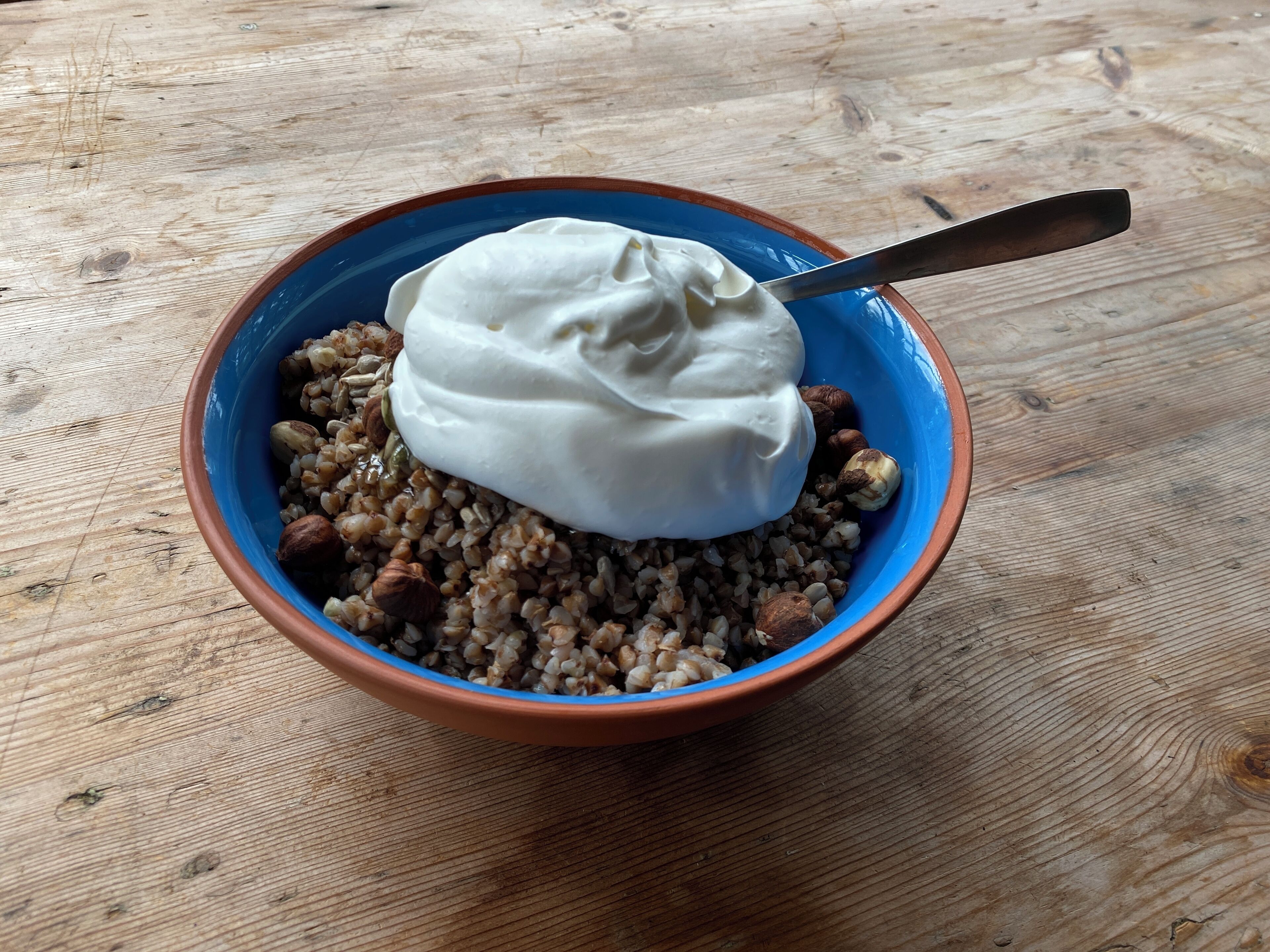 A bowl of porridge with nuts and a dollop of cream on a wooden table.