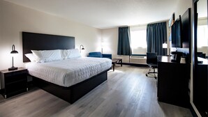 A modern hotel room with a large bed, a desk, a chair, and a flat-screen TV. - Surestay By Best Western Forsyth (Forsyth)