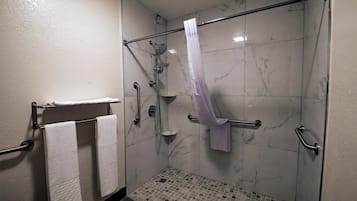 A shower area with a glass door, a handrail, a towel rack with two towels, and a showerhead.