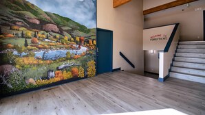 A hallway with a large mural of a landscape, a staircase, and a welcome sign. - Surestay By Best Western Forsyth (Forsyth)