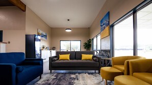 A modern living room with a sofa, armchairs, and a coffee table. There is a large window providing natural light and a view of the outdoors. - Surestay By Best Western Forsyth (Forsyth)