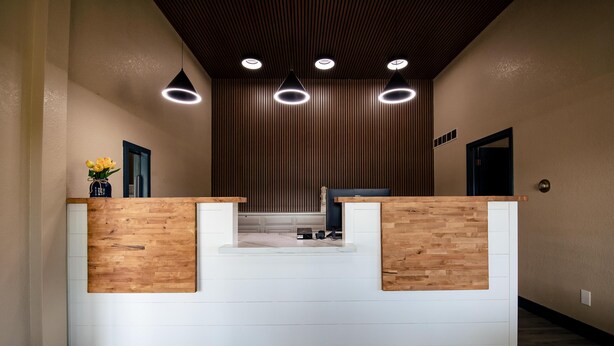 A reception desk with a wooden finish, a white counter, and a modern pendant light fixture. - Surestay By Best Western Forsyth (Forsyth)