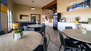 A modern dining area with round tables and chairs, a kitchen area with a refrigerator and counter, and artwork on the walls. - Surestay By Best Western Forsyth (Forsyth)