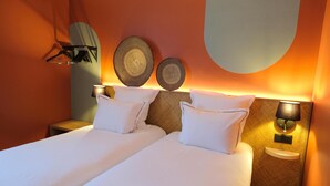 Una habitación de hotel con dos camas, un perchero en la pared, dos lámparas de pared y una mesita de noche pequeña.