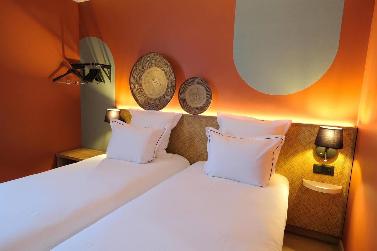 Une chambre d’hôtel avec deux lits, un porte-serviettes fixé au mur, deux lampes fixées au mur et une petite table de chevet.