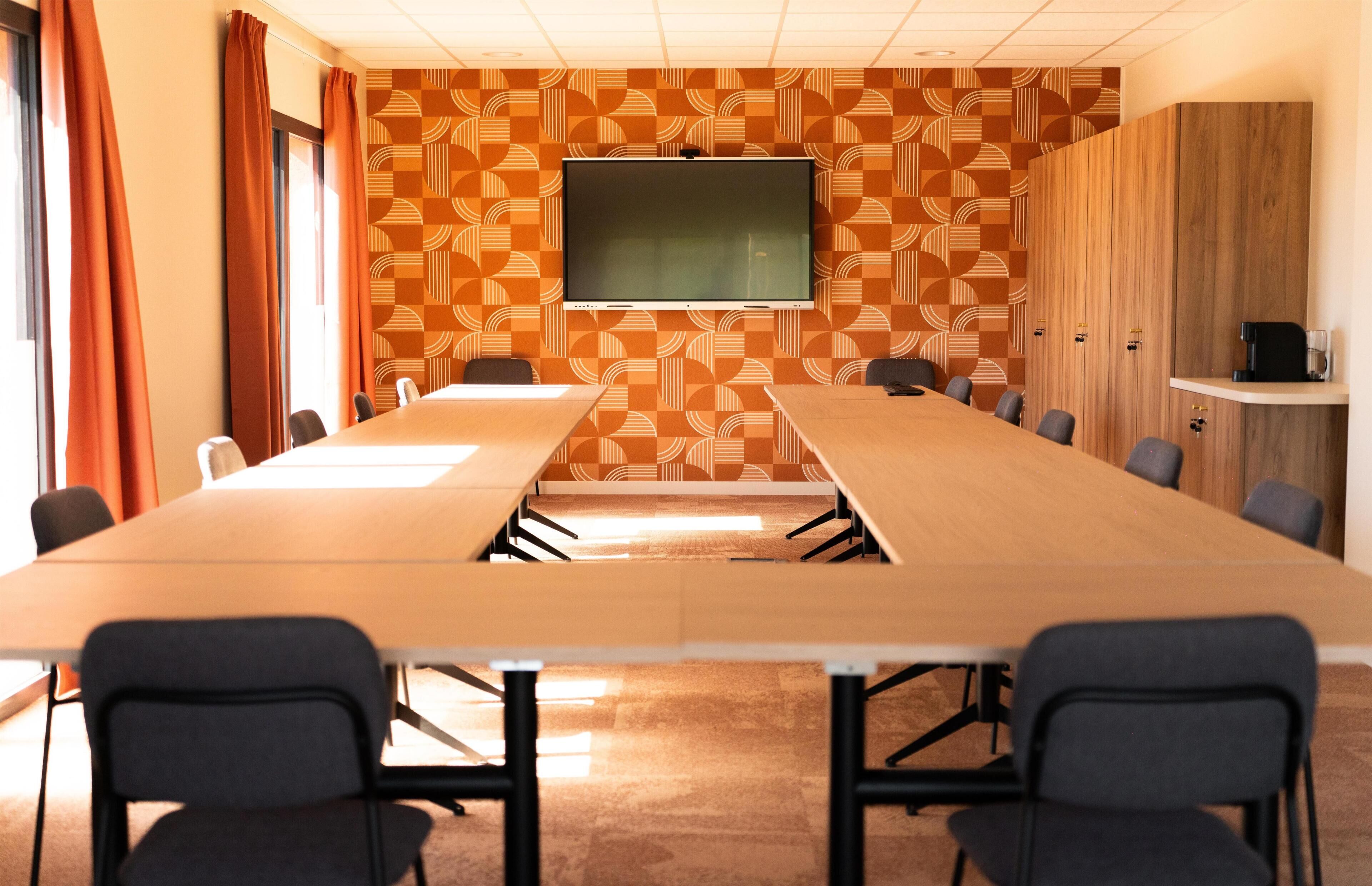 A conference room with a long table, chairs, a television, and a patterned wall.