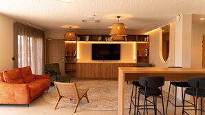 Una sala de estar moderna con un sofá, sillas, un televisor y una zona de bar con barra de madera.