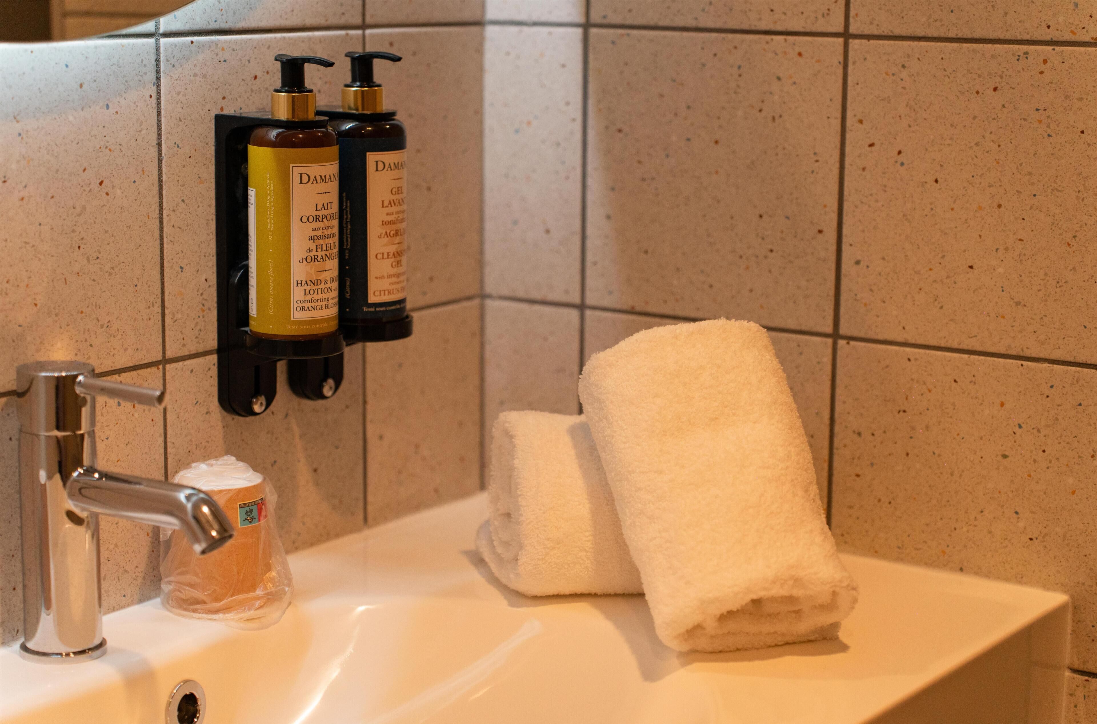 Un lavabo de salle de bain avec un flacon de savon liquide, une serviette et un flacon de shampoing.