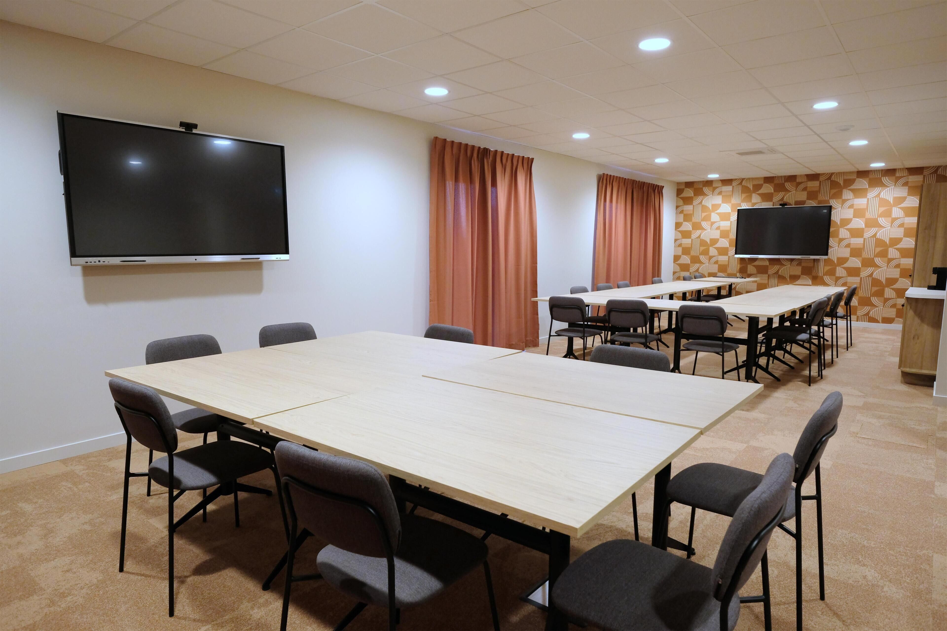 Un salón de conferencias con una gran mesa, sillas, un televisor y cortinas.