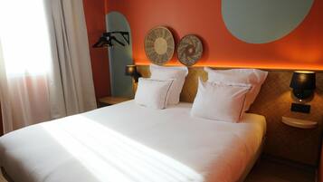 Uma cama bem arrumada com lençóis brancos, duas luminárias fixadas na parede e dois pratos decorativos na parede.