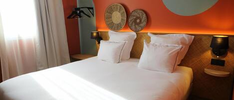 Una cama bien hecha con sábanas blancas, dos lámparas fijadas a la pared y dos platos decorativos en la pared.