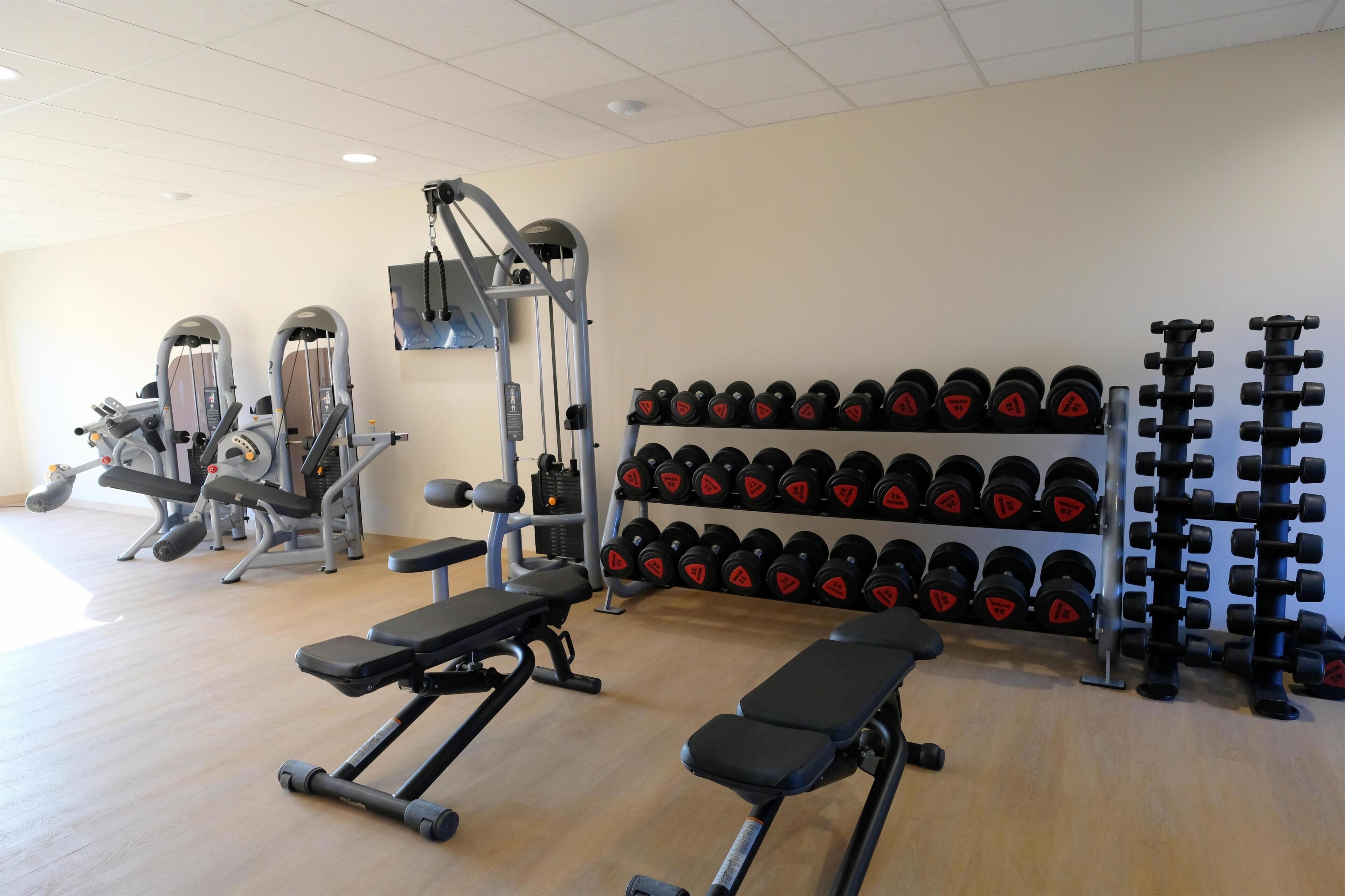 A gym with benches, weight machines, and racks of dumbbells.