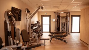 Un gimnasio con diversas máquinas de ejercicio, bancos y mancuernas.