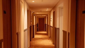 Un pasillo de hotel con puertas a ambos lados, pisos alfombrados y una puerta de madera al final.