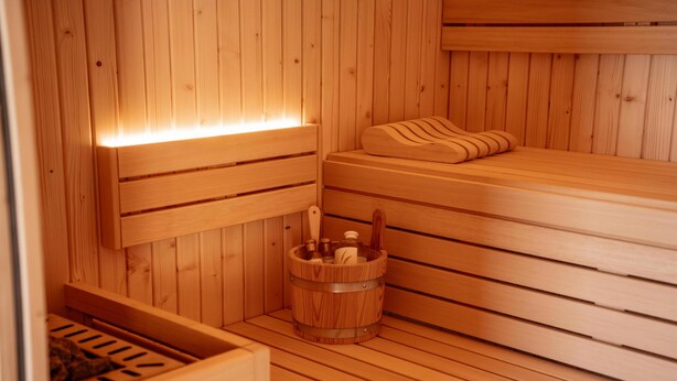 Una sauna de madera con bancos, un balde de madera y un banco con almohada.