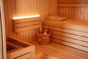 A wooden sauna with benches, a wooden bucket, and a bench with a pillow.