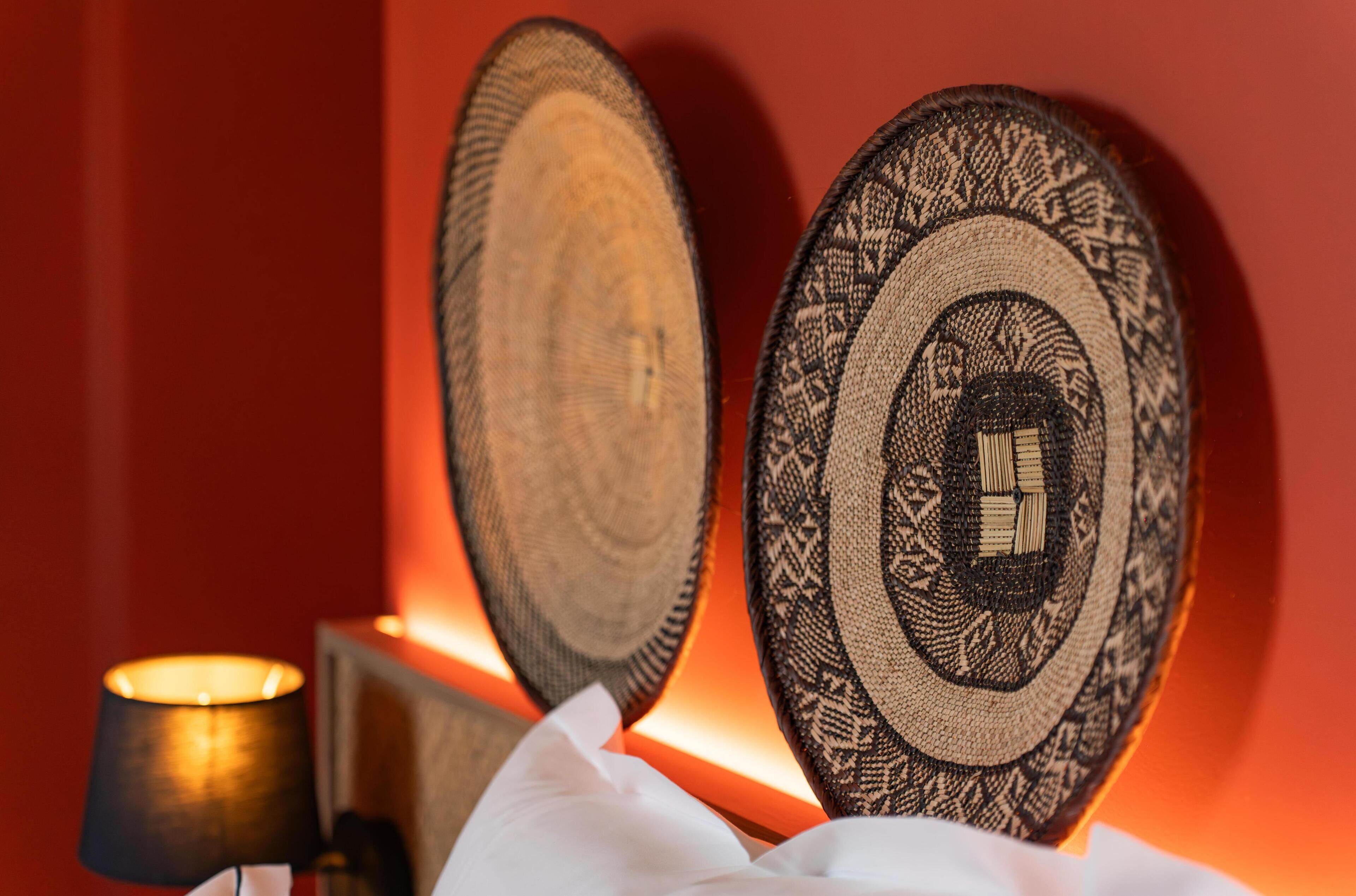 Zwei an der Wand befestigte dekorative Teller mit aufwendigen Mustern, eine Lampe und ein weißes Tuch auf einem Tisch.