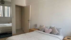 A bedroom with a large bed, a nightstand, a bedside lamp, and a door leading to another room.