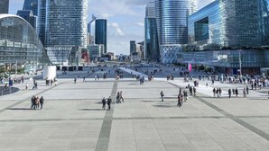 A modern urban plaza with contemporary architecture, including a large glass building and a curved structure.