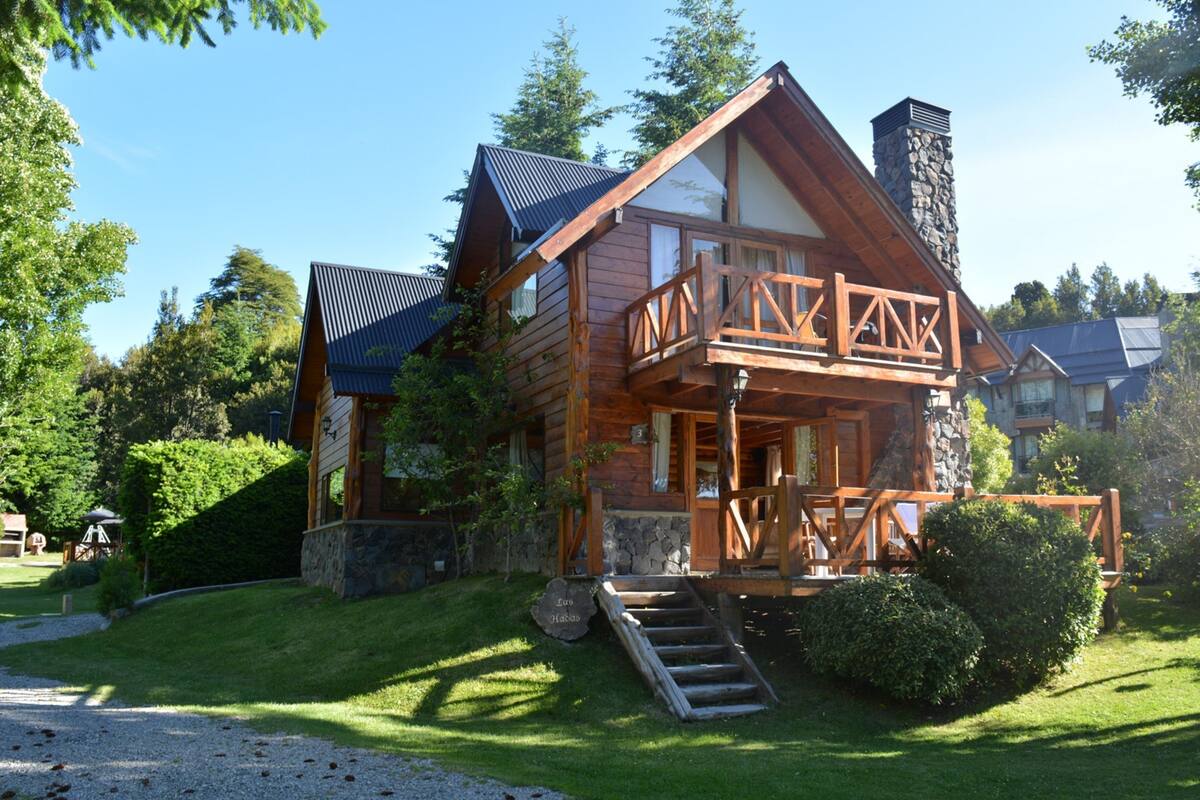 Une cabane en rondins avec une cheminée en pierre, une terrasse en bois et des fondations en pierre.