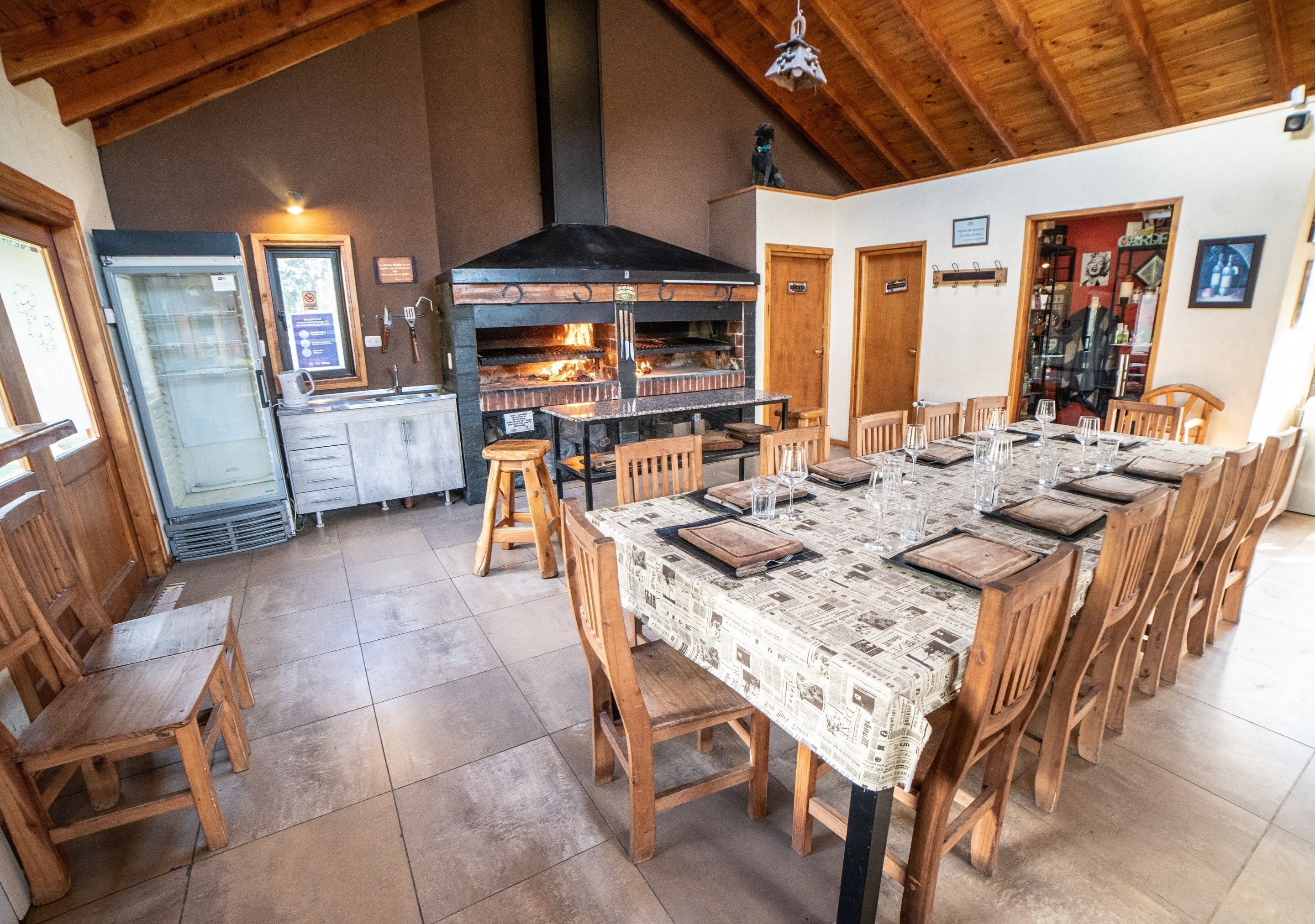 A rustic dining area with a long wooden table, wooden chairs, and a wood-burning oven.