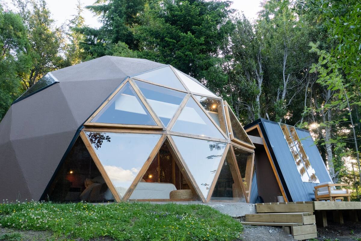 Une structure en forme de dôme géodésique, dotée de grandes fenêtres en verre et entourée d’une forêt.