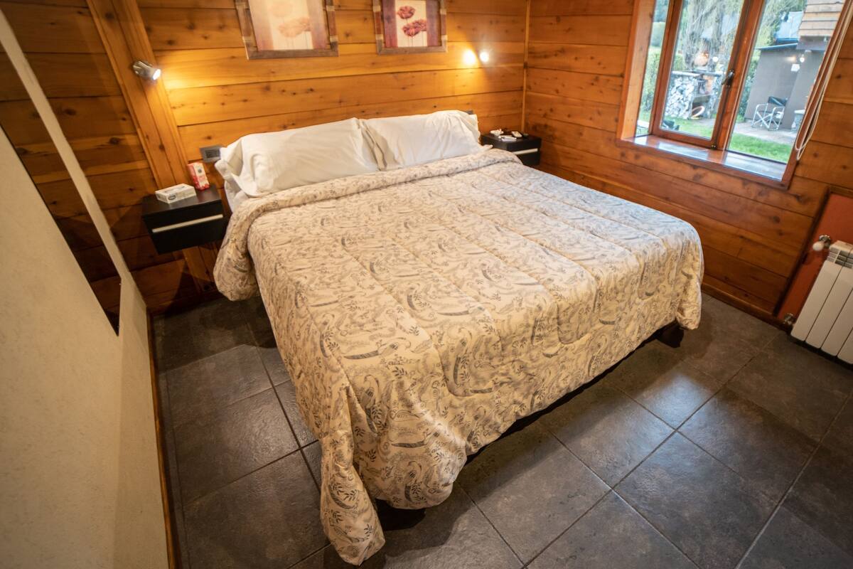 Une chambre dans une cabane en bois, avec un lit, une table de chevet et une fenêtre.