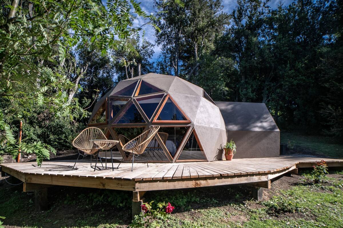 Une structure en forme de dôme géodésique, dotée d’une terrasse en bois et de deux fauteuils en osier.