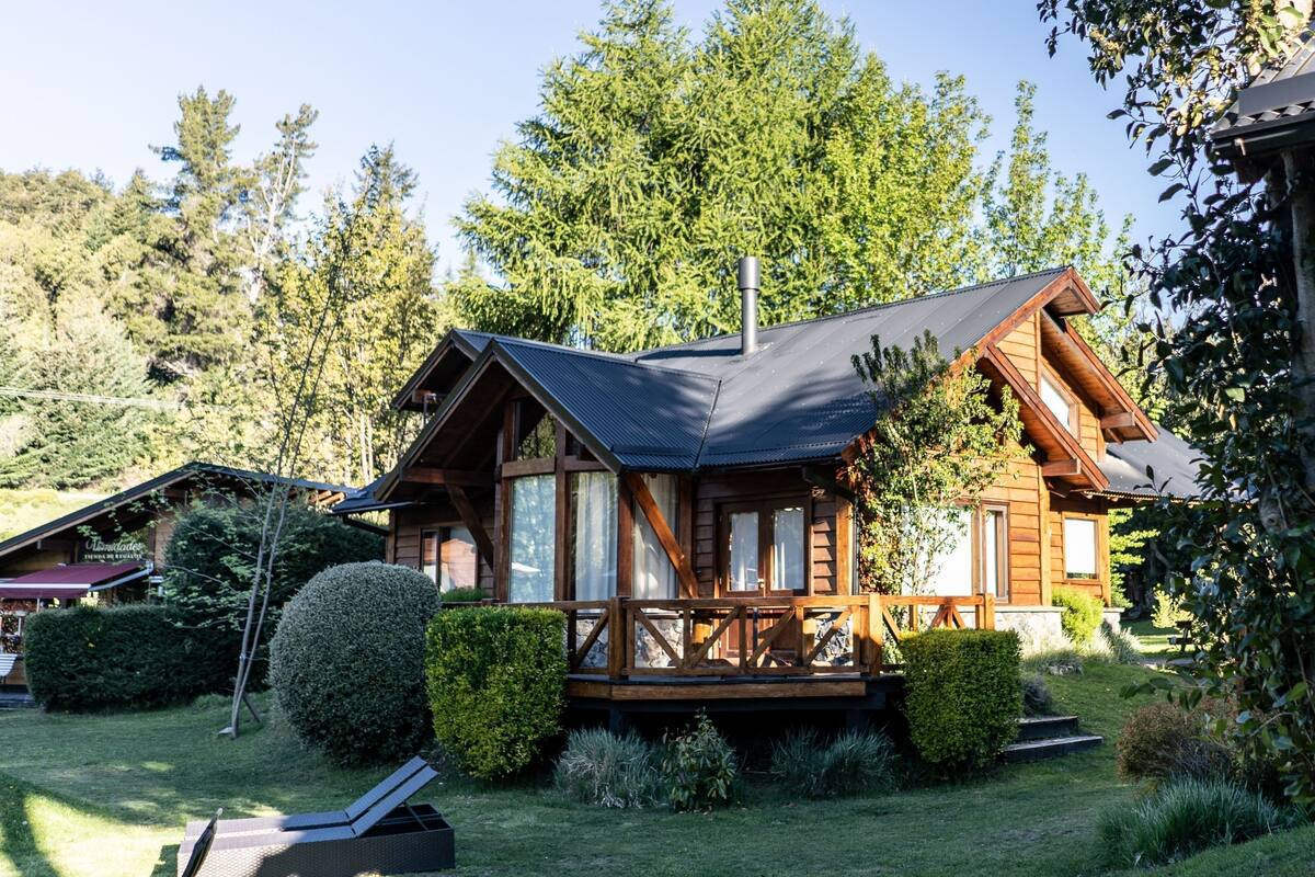 Une cabane en bois dotée d’une terrasse, entourée de jardins et d’arbres bien entretenus.